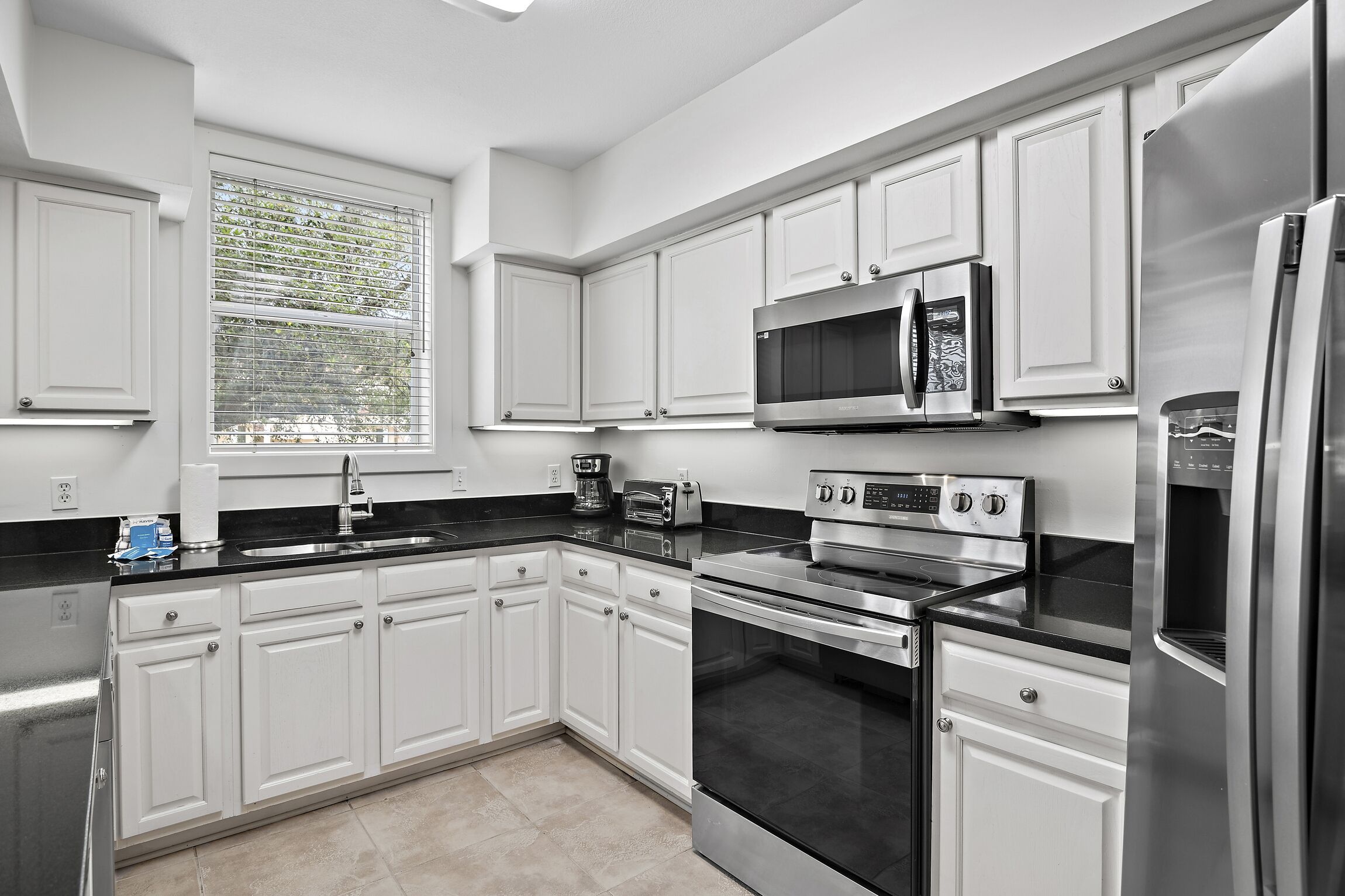 A modern kitchen with white cabinets, a stainless steel refrigerator, a microwave, and a stove.