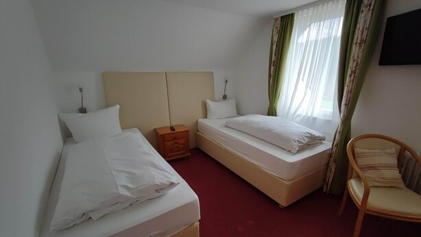 A hotel room with two beds, a wooden nightstand, a chair, and a TV mounted on the wall.