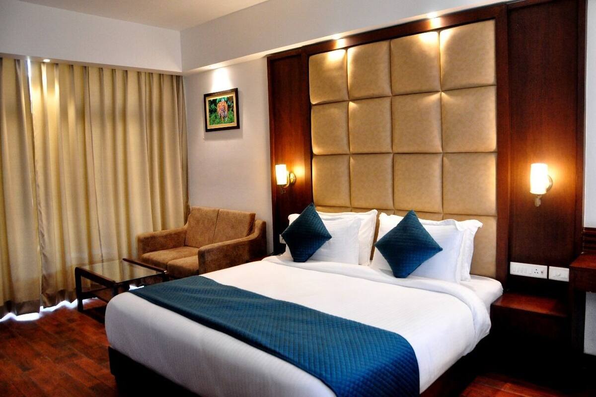 A hotel room with a large bed, a wooden headboard, a sofa, a glass coffee table, and a picture on the wall.