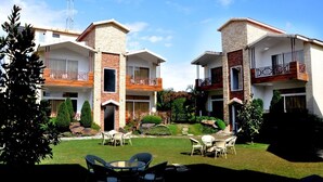 A modern multi-story building with balconies, a well-maintained garden, and outdoor seating.