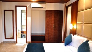A hotel room with a bed, a wardrobe, a mirror, and an air conditioning unit.