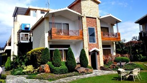 A two-story house with a balcony, a stone facade, and a well-maintained garden.