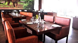 A restaurant with long wooden tables and red leather booths, a tiger mural on the wall, and a view of the outdoors.