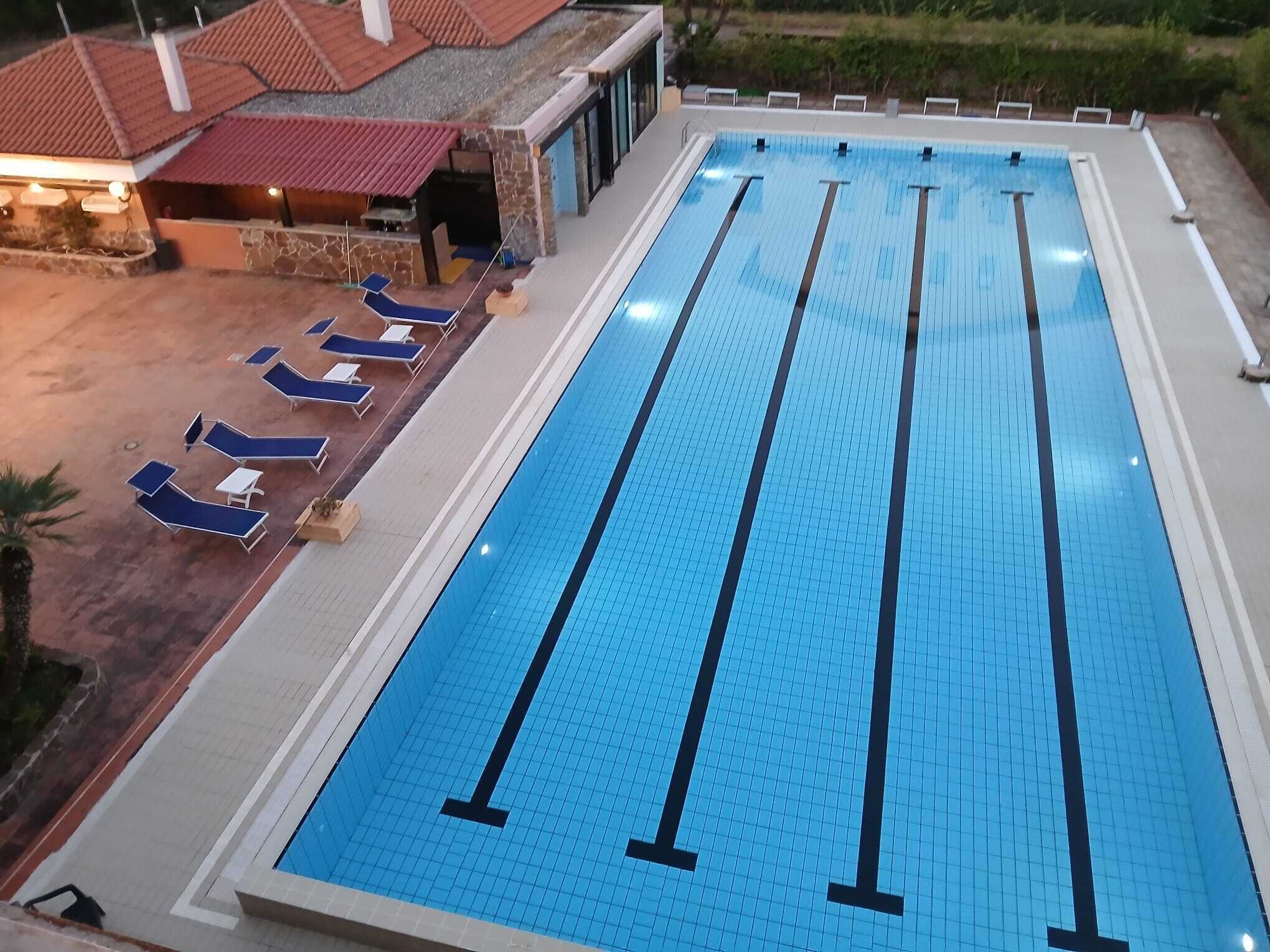 Una gran piscina cubierta con varias pistas, tumbonas y una zona techada con techo rojo.