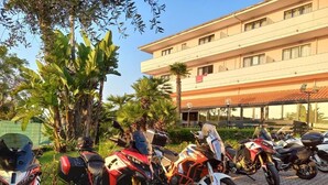 A row of parked motorcycles in front of a building with a tiled roof and multiple windows. - Green Sporting Club Hotel (Alghero)