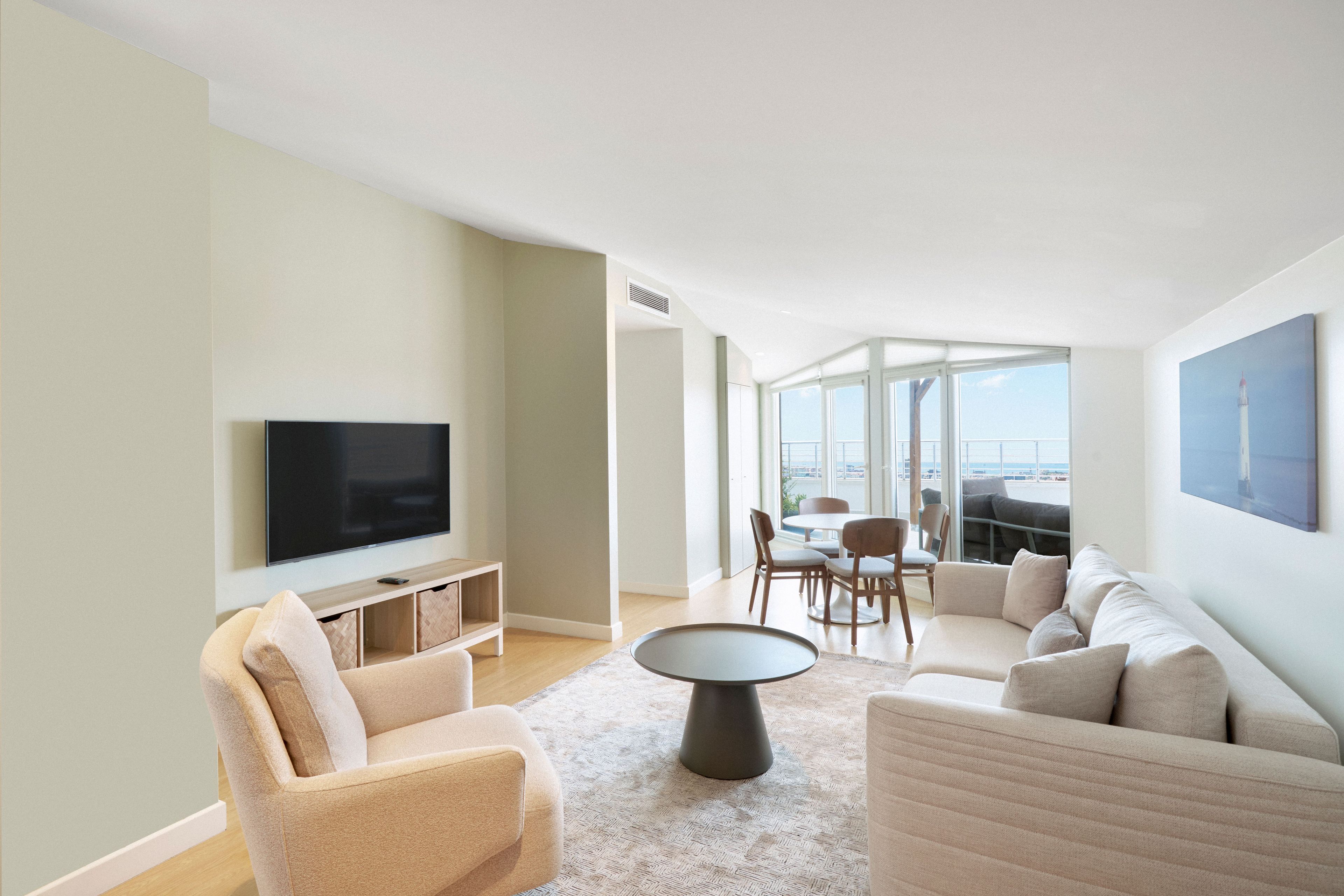 A modern living room with a flat-screen TV, a sofa, a coffee table, and a dining area with chairs.
