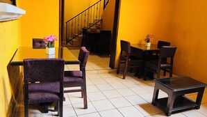 Un coin repas avec des chaises à revêtement violet, une petite table ornée d’un vase de fleurs et un escalier en arrière-plan.