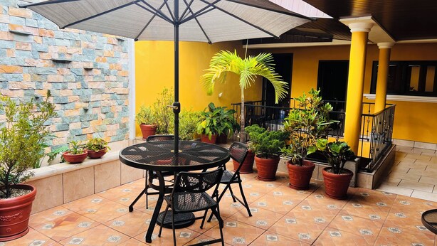 Un espace patio avec une table ronde et des chaises, entouré de plantes en pot et d’un mur de pierre.