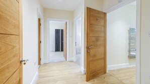 A hallway with wooden doors, a white wall, and a tiled floor. - Luxury 3 Bedroom Apartment with Parking (Maidenhead)
