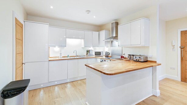 A modern kitchen with white cabinets, a wooden countertop island, and a built-in microwave. - Luxury 3 Bedroom Apartment with Parking (Maidenhead)