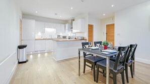 A modern kitchen with white cabinets, a central island, and a dining area with a table and chairs. - Luxury 3 Bedroom Apartment with Parking (Maidenhead)