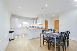 A modern kitchen with white cabinets, a central island, and a dining area with a table and chairs.