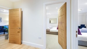 A hotel room with a wooden wardrobe, a bed with a white duvet, and a small bedside table. - Luxury 3 Bedroom Apartment with Parking (Maidenhead)