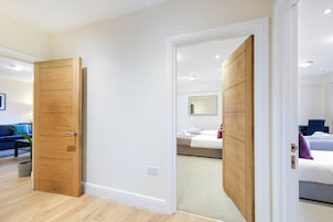 A hotel room with a wooden wardrobe, a bed with a white duvet, and a small bedside table.