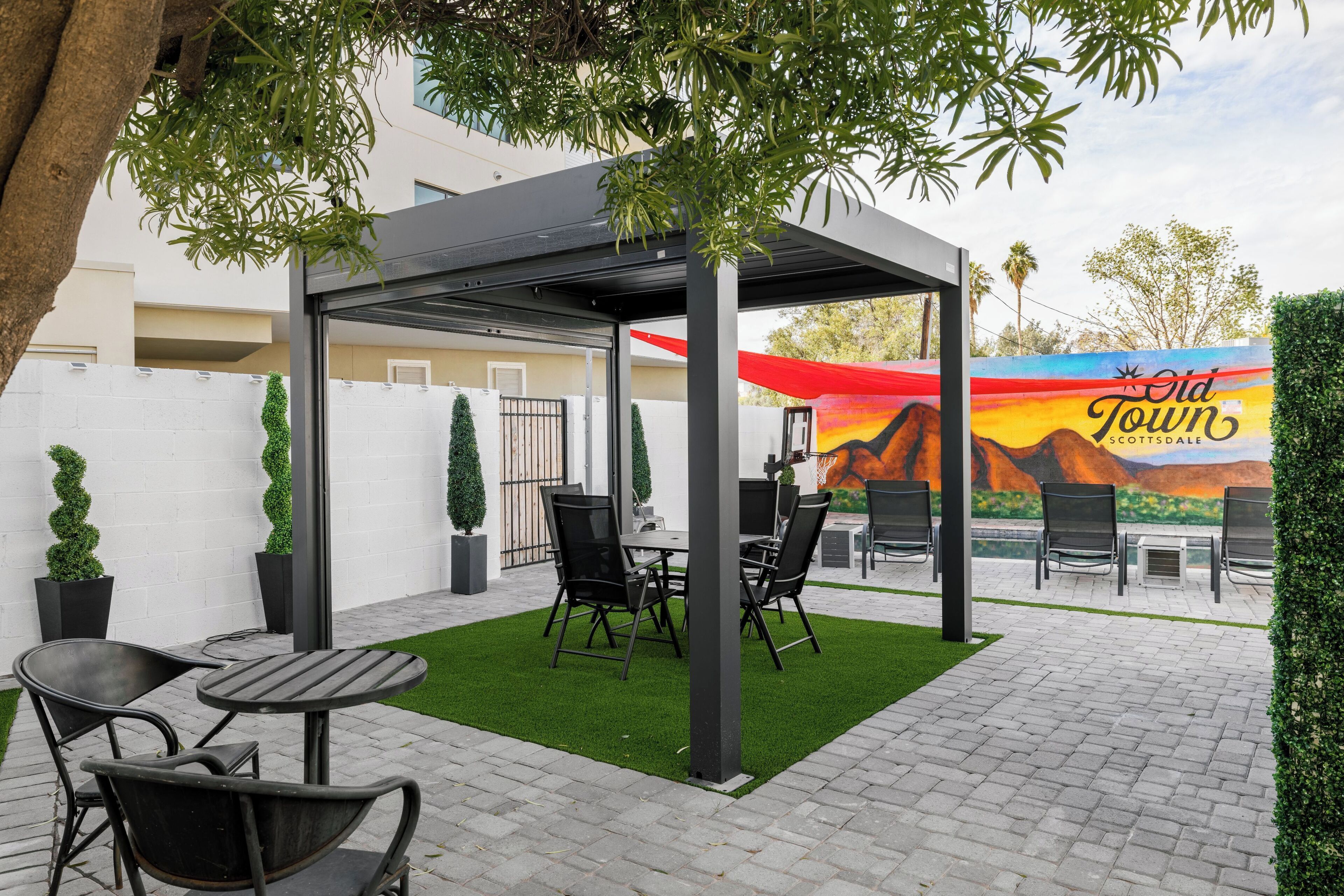 An outdoor patio area with a covered seating area, a mural in the background, and a landscaped garden.