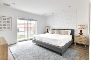 A modern bedroom with a large bed, a patterned rug, a wooden nightstand, and a wall with geometric patterns.