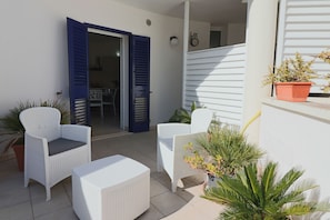 Une terrasse dotée de meubles en osier peints en blanc, d’une porte bleue et de plantes en pot.