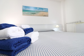 Un lit bien fait, avec des serviettes pliées, un tableau représentant une plage accroché au mur et un radiateur.