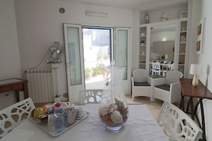 Une pièce comprenant une table à manger, des chaises, un radiateur, un ventilateur, une fenêtre donnant sur un beau paysage et un fauteuil en osier blanc.
