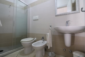 Ein Badezimmer mit Duschkabine aus Glas, Toilette, Bidet und Waschbecken mit Spiegel darüber.