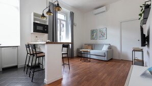 A modern kitchen with a microwave, a dining area with chairs, a grey sofa, and a small table. - Italianway - Umbria 50 B (Milan)