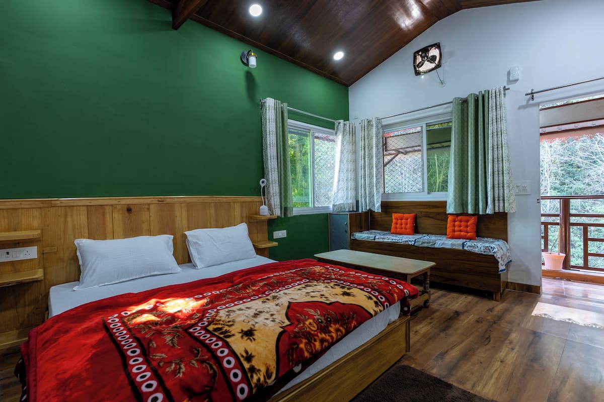 A room with a bed, a wooden bench, a small table, and a window with curtains.