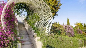 A staircase with a white lattice structure on the left, surrounded by lush greenery and flowering plants. - Santa Barbara Mesa Home on the hill (Santa Barbara)