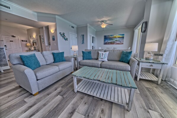 A living room with a grey sofa, teal cushions, a wooden coffee table, and a painting on the wall. - Gulf Crest 2305 | Beachfront Penthouse with Stunning Views (Panama City)