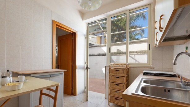 A kitchen with a wooden table, a sink, and a window with a view of palm trees. - 3797 Casa di Marì by Barbarhouse (Melendugno)