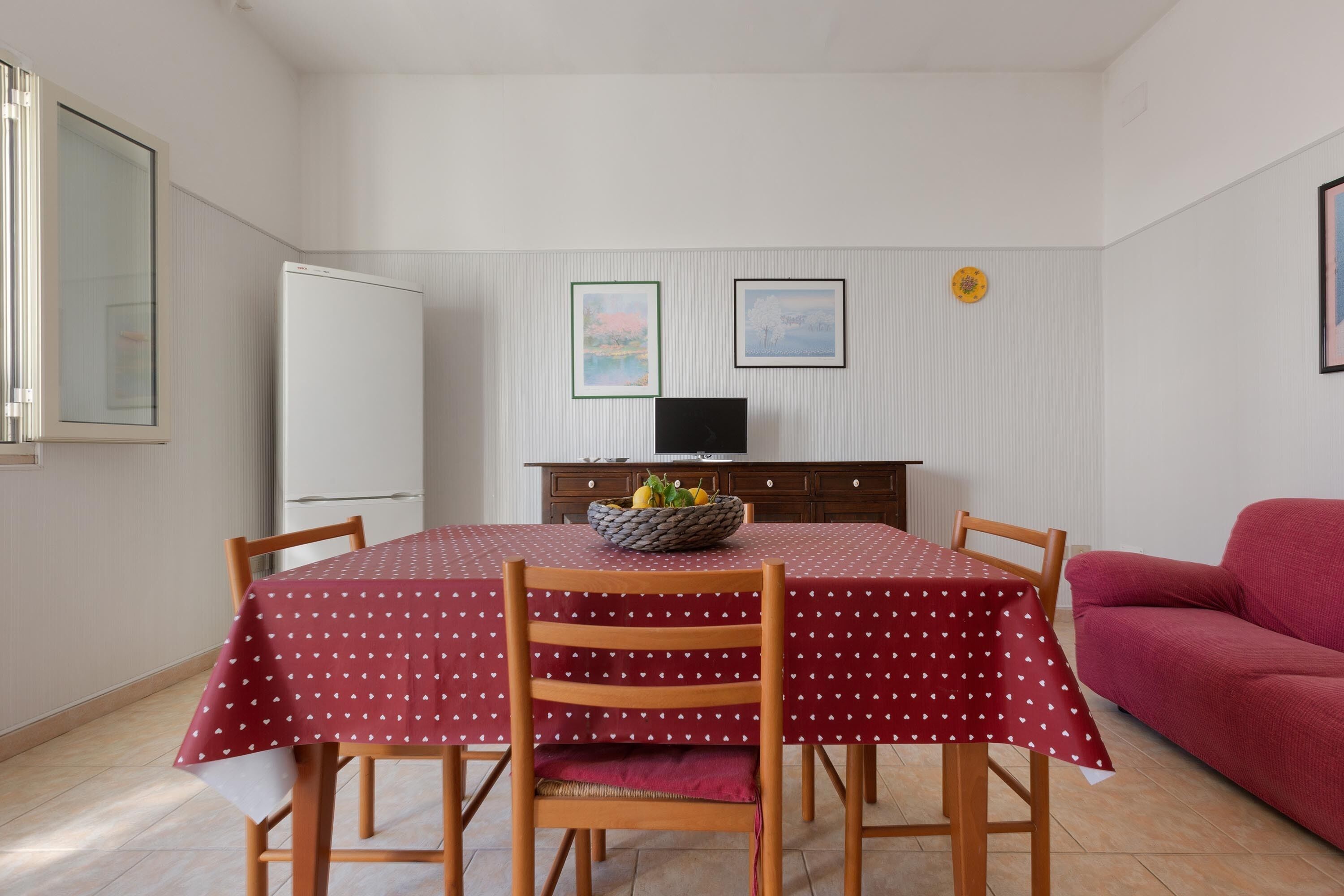 Ein Essbereich mit einem Tisch, bedeckt mit einer roten Tischdecke mit weißen Mustern, umgeben von Holzsesseln.