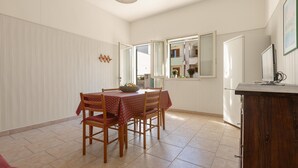 A dining area with a wooden table and chairs, a white radiator, and a window with an open door. - 3797 Casa di Marì by Barbarhouse (Melendugno)
