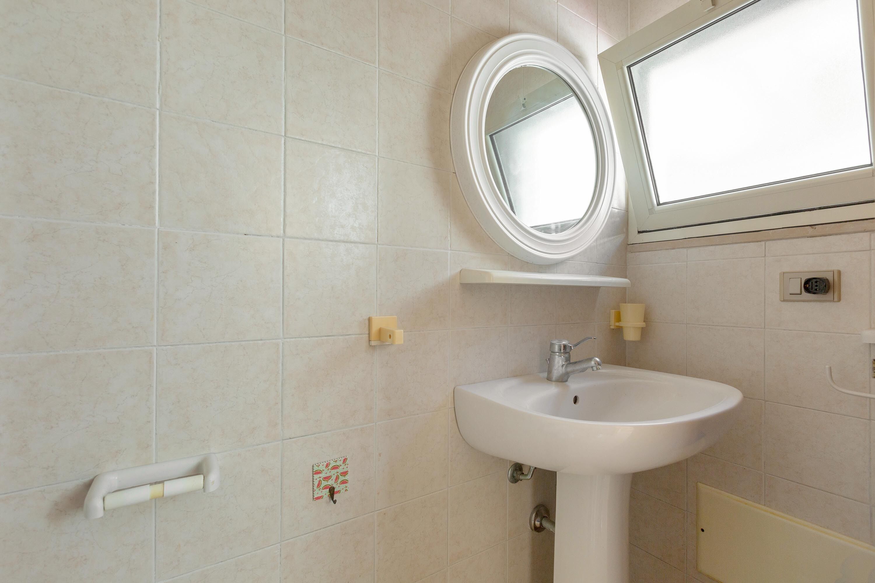 A bathroom with a white sink, a mirror, and a window.