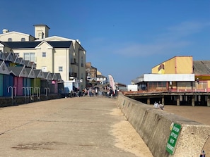 A coastal promenade with colorful beach huts, a concrete barrier, and buildings with balconies.