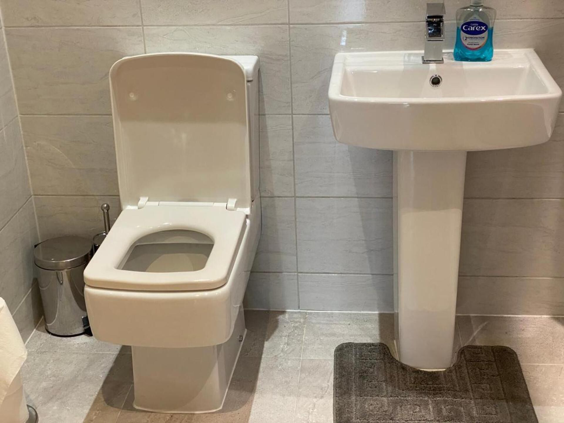A bathroom with a toilet, a sink, and a trash can.