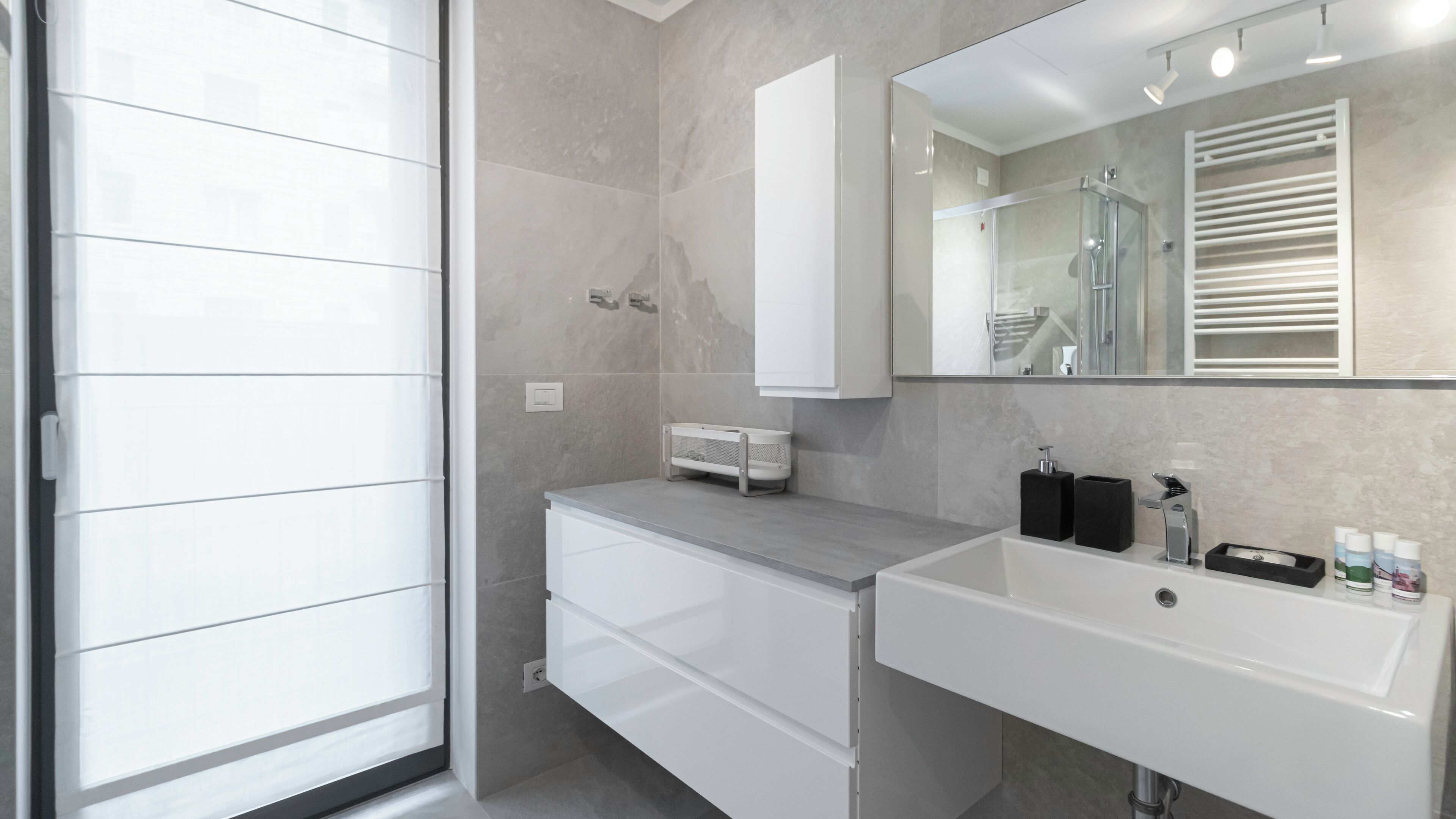 A modern bathroom with a large mirror, a white sink, and a shower area.