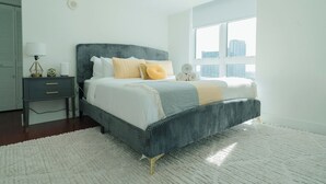 A modern bedroom with a large bed, a bedside table, and a window with a city view.