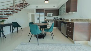 A modern kitchen with dark cabinets, stainless steel appliances, and a dining area with teal chairs and a round table.