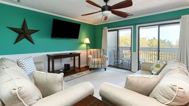 Un salon aux murs de couleur turquoise, doté d’un ventilateur de plafond, d’un téléviseur, d’un fauteuil à rayures, d’un canapé et offrant une vue sur l’extérieur grâce à une porte-fenêtre coulissante.