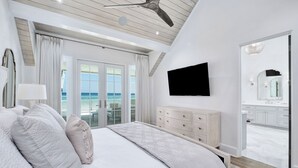 Ein Schlafzimmer mit einem großen Bett, einem Deckenventilator, einem Fernseher und Meerblick durch die Glastüren.