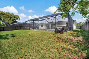 Un espacio exterior cubierto con piscina, rodeado por un patio cercado y árboles.