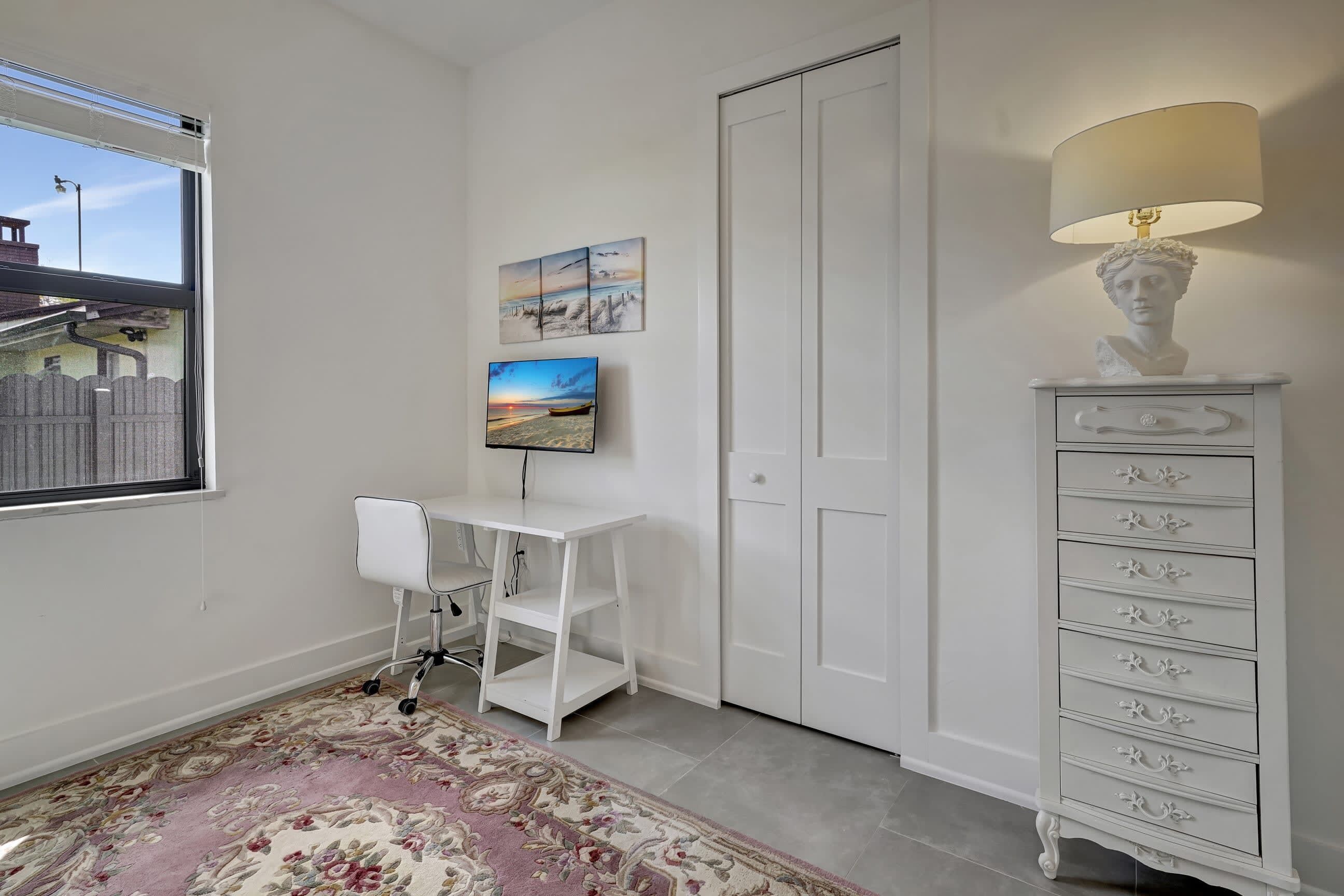 A room with a white desk, a chair, a desk lamp, a decorative bust, and a painting on the wall.