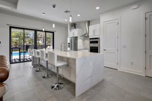 A modern kitchen with a marble island, stainless steel appliances, and a view of a swimming pool.