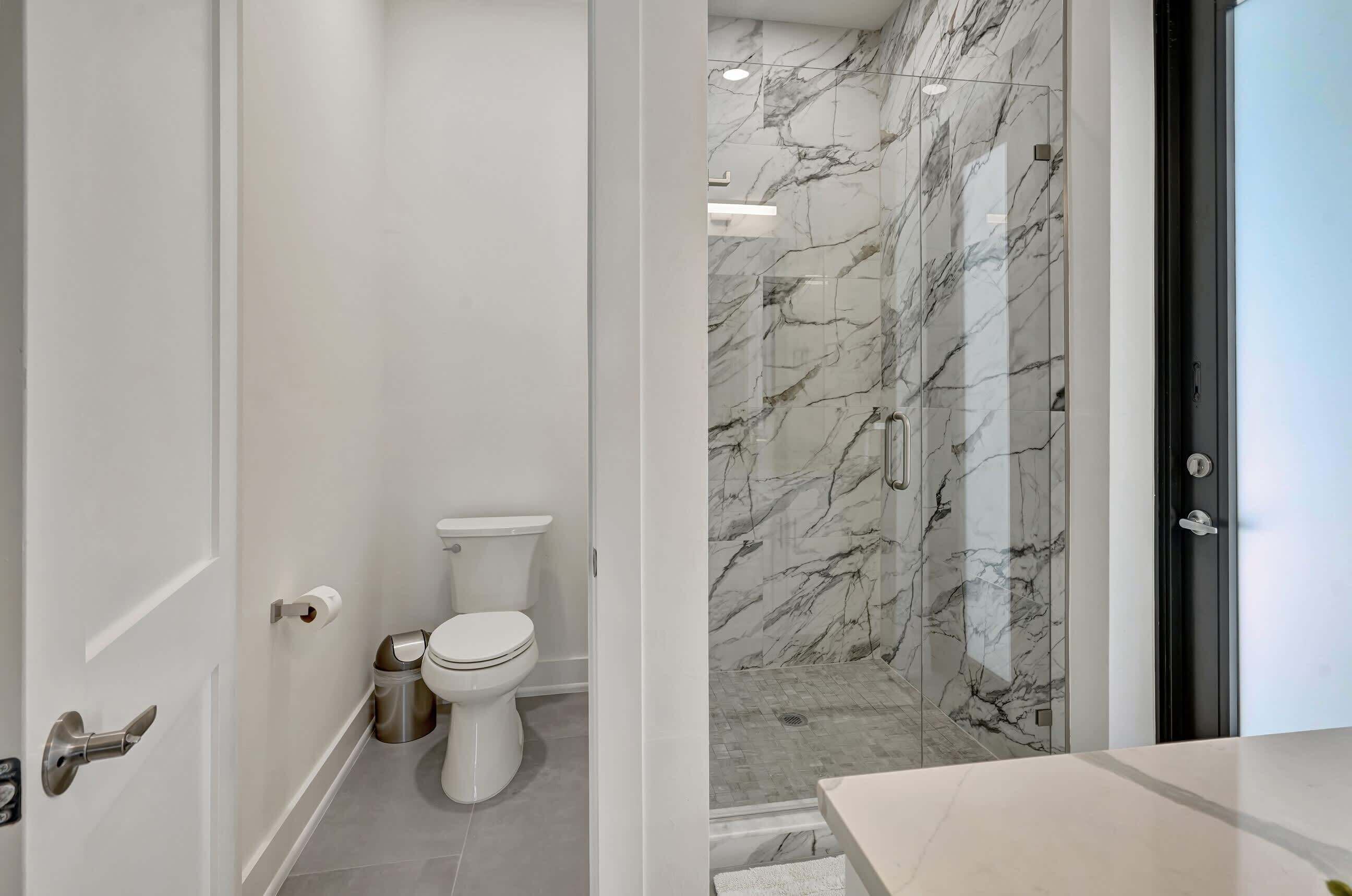 Et badeværelse med toilet, skraldespand og bruser med marmorvægge.