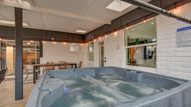 A modern spa area with a hot tub, seating area, and a view of the kitchen through a glass door.