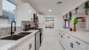 A modern kitchen with white cabinetry, a double sink, a stove, and a microwave.
