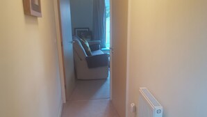 A hallway with a patterned rug, a radiator, and a door leading to a living area with a sofa.