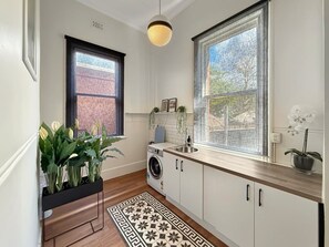 A compact kitchen with a washing machine, a sink, and a window with a view of a brick wall.