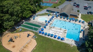 Eine Vogelperspektive zeigt einen Ferienort mit einem großen Schwimmbad, mehreren Tennisplätzen und einem Sandspielbereich.