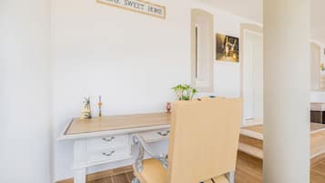 Et værelse med et hvidt skrivebord, en stol med en stribet pude, et skilt på væggen med teksten 'HOME SWEET HOME' og et indrammet billede.