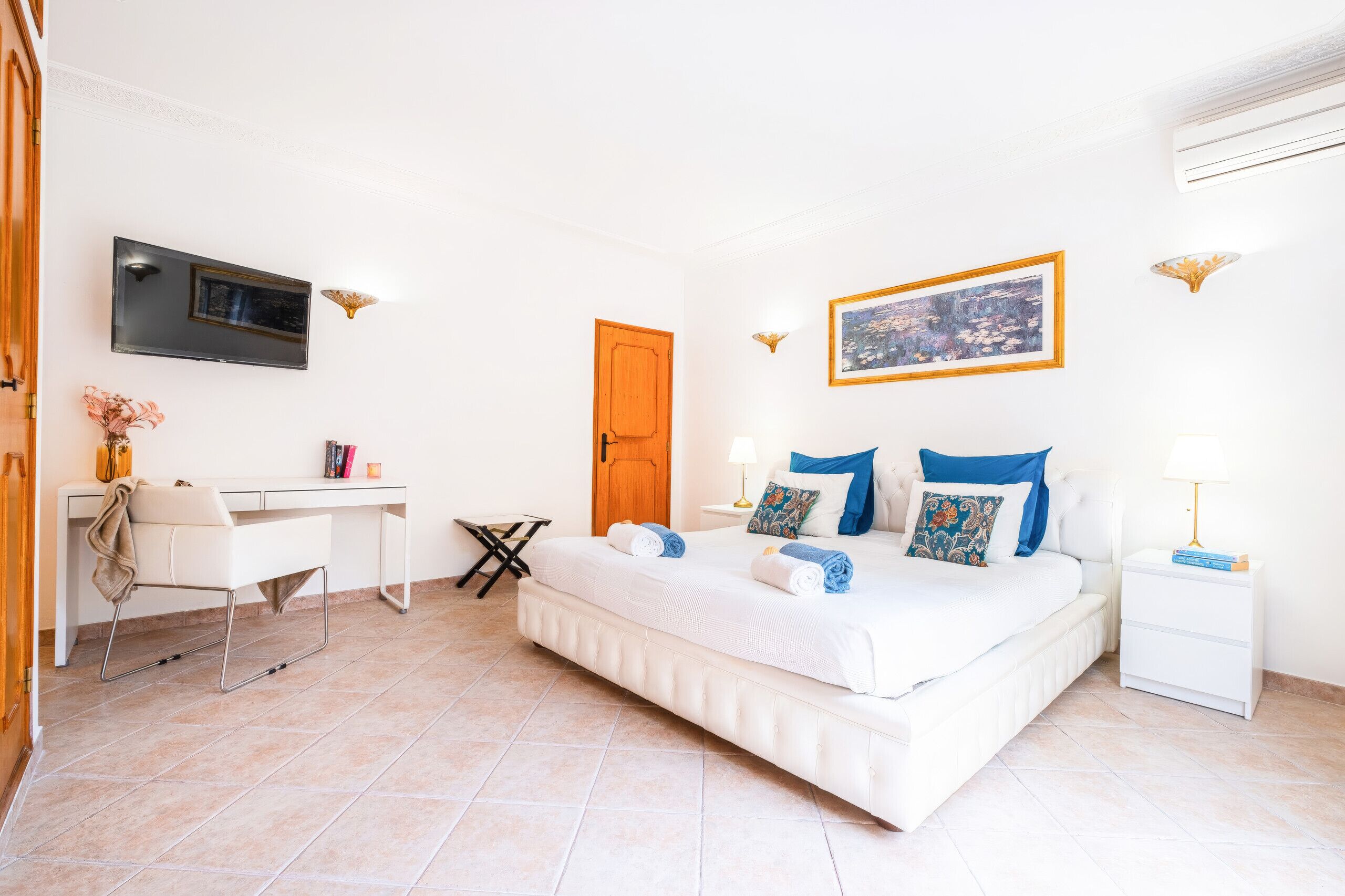 Habitación de hotel con cama, escritorio, silla, televisor y un cuadro en la pared.
